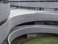 a circular building with concrete steps and an open lawn area beside it by some buildings