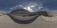 three circular cement objects sit on the ground near the grass and buildings, with blue skies and clouds behind