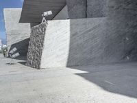 a large, concrete wall with a camera on top and some people walking by next to it