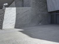 a large, concrete wall with a camera on top and some people walking by next to it