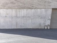 the skateboarder is attempting to stop in front of an empty concrete building with a wall