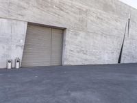 there is a parking garage and some trash cans outside of it, with a long wall in the background