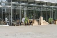 a store front with large windows, plants and cardboard boxes stacked on the floor outside