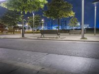 the empty street next to a bench with lights on it at night, illuminated with bright street lighting