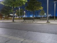 the empty street next to a bench with lights on it at night, illuminated with bright street lighting