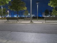 the empty street next to a bench with lights on it at night, illuminated with bright street lighting