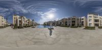 an upside down view of a swimming pool with two buildings behind it, and a fisheye lens over the pool