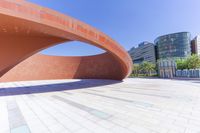 a curved brick structure sitting inside of a courtyard area with a white building in the background