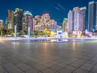 a city view at dusk looking toward a park with fountains and buildings in the background