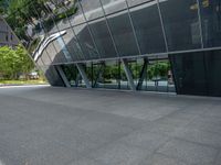 a gray tiled building with a curved glass exterior and sidewalk and trees in front of it