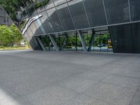 a gray tiled building with a curved glass exterior and sidewalk and trees in front of it