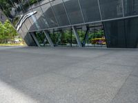 a gray tiled building with a curved glass exterior and sidewalk and trees in front of it