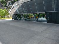 a gray tiled building with a curved glass exterior and sidewalk and trees in front of it