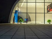 an empty lobby with many plants in it at night time / and very light coming through the windows