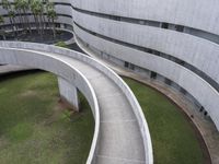 a concrete building and walkway with curved walls leading into the building and trees at either side of it