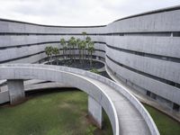 a concrete building and walkway with curved walls leading into the building and trees at either side of it