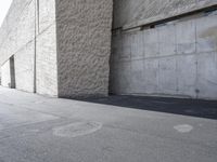 a young boy on a skateboard riding down the curb of an empty building where concrete meets wall