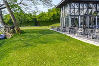 a glass building with an outside seating area for picnics and lawn furniture on grass