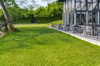 a glass building with an outside seating area for picnics and lawn furniture on grass