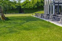 a glass building with an outside seating area for picnics and lawn furniture on grass