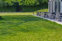 a glass building with an outside seating area for picnics and lawn furniture on grass