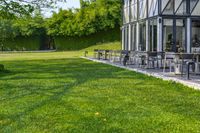 a glass building with an outside seating area for picnics and lawn furniture on grass