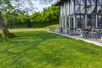 a glass building with an outside seating area for picnics and lawn furniture on grass