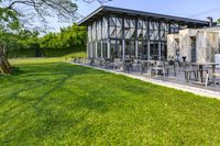 a glass building with an outside seating area for picnics and lawn furniture on grass