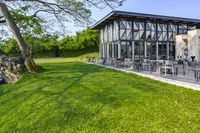 a glass building with an outside seating area for picnics and lawn furniture on grass