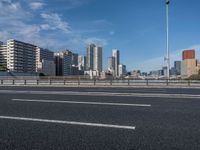 a road with tall buildings in the background and water under a blue sky near it