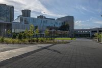 a city street surrounded by grass and tall buildings at the end of a street there is a paved pathway in front of the building