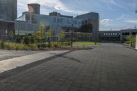 a city street surrounded by grass and tall buildings at the end of a street there is a paved pathway in front of the building