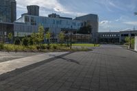 a city street surrounded by grass and tall buildings at the end of a street there is a paved pathway in front of the building