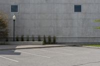 an empty parking lot next to a tall building in a parking lot with trees growing on the ground