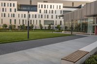 a city street surrounded by grass and tall buildings at the end of a street there is a paved pathway in front of the building