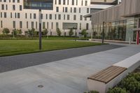 a city street surrounded by grass and tall buildings at the end of a street there is a paved pathway in front of the building