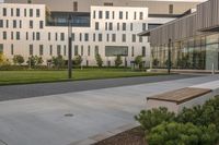 a city street surrounded by grass and tall buildings at the end of a street there is a paved pathway in front of the building