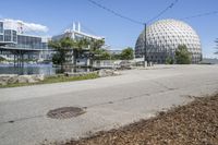 a big ball surrounded by some buildings on a lot near water and trees and grass