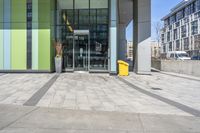 a yellow object sitting on the sidewalk next to the entrance to a large building in a city