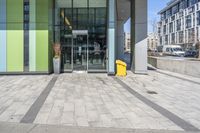 a yellow object sitting on the sidewalk next to the entrance to a large building in a city