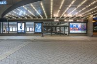 a bus stop at the entrance to a cinema theater with lights on and two people standing under it