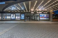 a bus stop at the entrance to a cinema theater with lights on and two people standing under it