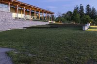 a large stone wall sitting in the middle of a grass field by a building with a walkway