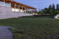 a large stone wall sitting in the middle of a grass field by a building with a walkway