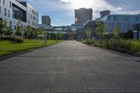 a city street surrounded by grass and tall buildings at the end of a street there is a paved pathway in front of the building