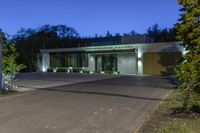 a green and white building next to a parking lot at night with trees lining the sidewalk