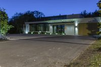 a green and white building next to a parking lot at night with trees lining the sidewalk