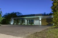 a green and white building next to a parking lot at night with trees lining the sidewalk