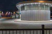 the round building is near two large poles that are at night time and lit by street lights