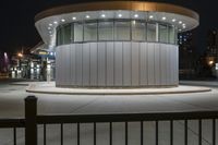 the round building is near two large poles that are at night time and lit by street lights